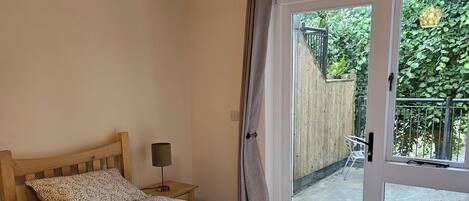 Un dormitorio con dos camas, una mesita de noche, una lámpara y un ventanal corredero que da a un espacio exterior.