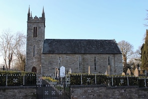 A historic stone church with a tall tower, a gated entrance, and a clear sky.