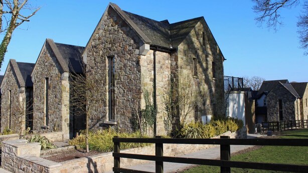 A stone building with a triangular roof, likely a church or chapel, with a wooden fence in the foreground. - Cosy Lakeside Retreat in Mountshannon (Mountshannon)