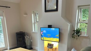 A living room with a TV, a wooden coffee table, a black leather sofa, a fireplace, and a window with a plant. - Cosy Lakeside Retreat in Mountshannon (Mountshannon)
