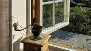Een raam met uitzicht op een landschap, een rustiek houten voorwerp en een metalen pot op een klein platform.