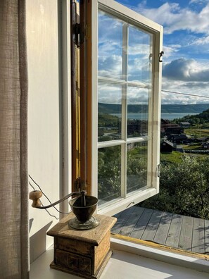 Ein Fenster mit Blick auf eine Landschaft, ein rustikales Holzobjekt und ein Metalltopf auf einer kleinen Plattform.