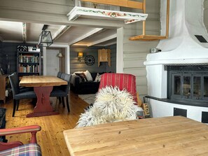 Ein gemütliches Wohnzimmer mit einem Holztisch, einer Couch, einem Kamin, einem Bücherregal und einer Lampe.