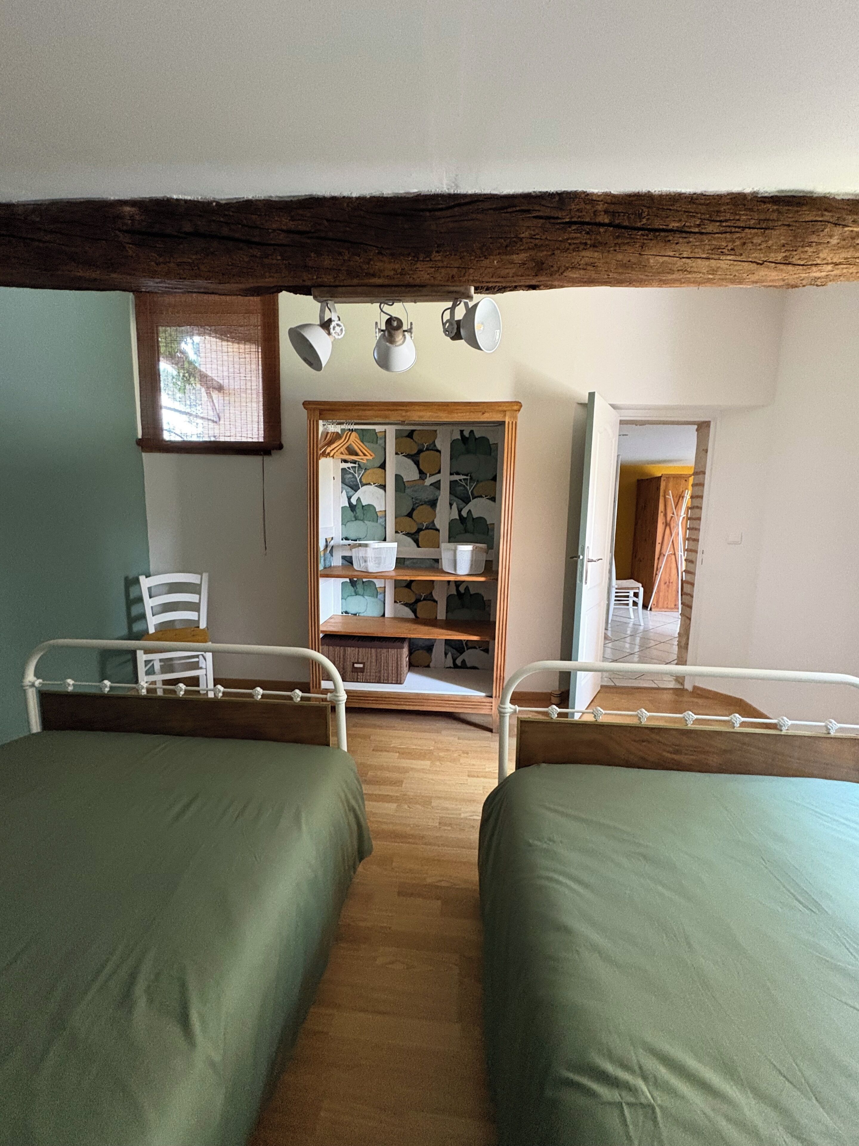 A room with two beds, a wooden cabinet, and a window with blinds.