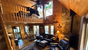 Un intérieur de chalet chaleureux avec une chambre en mezzanine, une cheminée en pierre et un coin repas.