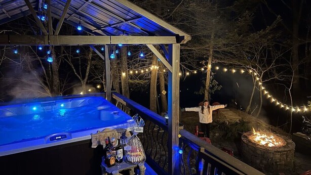 Un bain à remous doté d’une terrasse en bois, entouré d’arbres et illuminé de guirlandes lumineuses.