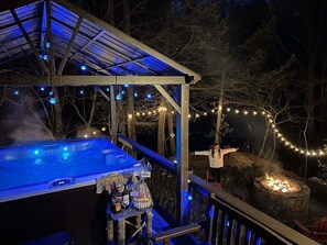 A hot tub with a wooden deck, surrounded by trees and string lights.