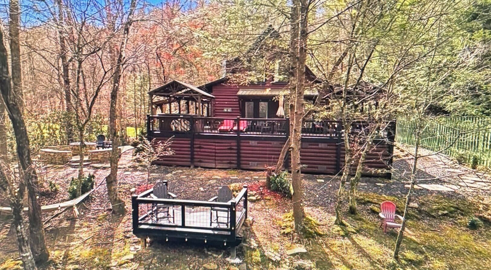 Une cabane dotée d’une terrasse, entourée d’arbres et d’une zone délimitée par une clôture.