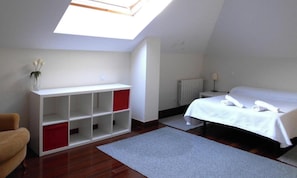 Ein Schlafzimmer mit Dachfenster, einem Bett, einem weißen Kleiderschrank und einem kleinen Tisch mit einer Lampe.