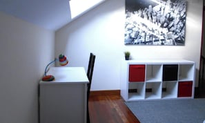 Ein Zimmer mit einem weißen Schreibtisch, einem Stuhl, einem roten und weißen Stauraum und einem Schwarz-Weiß-Foto an der Wand.