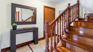 Una escalera de madera con barandilla, una consola oscura con espejo y una planta en maceta.