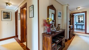 Um corredor com piso de madeira, um console de madeira com espelho, obras de arte emolduradas e um vaso com flores.