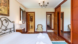 Quarto de hotel com uma cama grande, um candelabro, um guarda-roupa de madeira e um espelho.