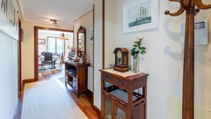 Um corredor com um cabideiro de madeira, um relógio e um quadro na parede.