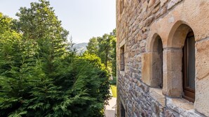 Um edifício de pedra com janelas em arco e vista para vegetação exuberante e colinas distantes.