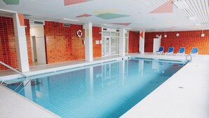 Une piscine intérieure avec un sol carrelé, une bouée de sauvetage et une porte donnant sur une autre pièce.