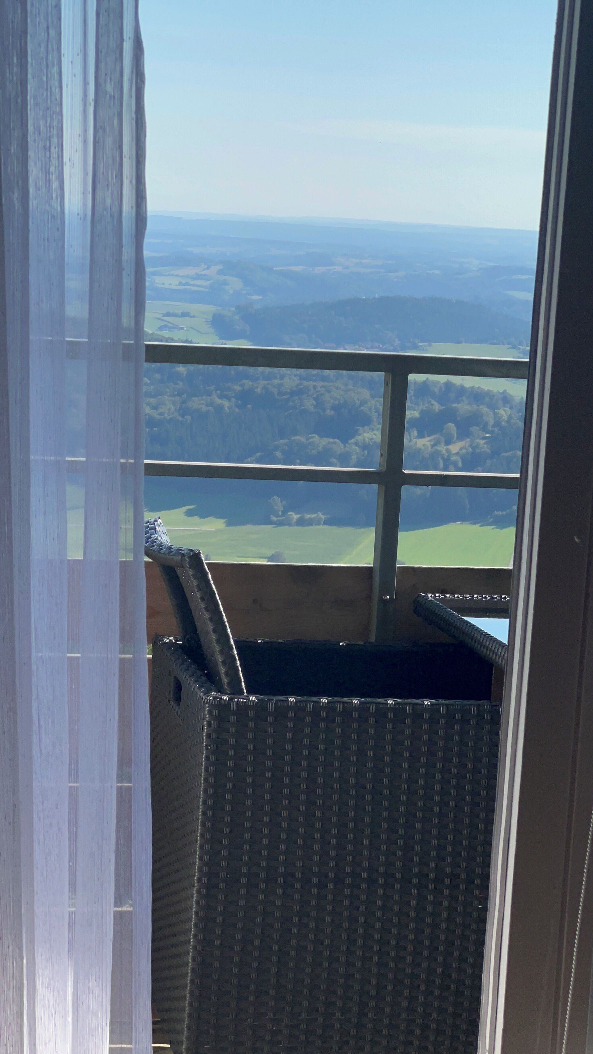 Un balcón con vistas a un paisaje, una silla de mimbre y una ventana que da al campo.