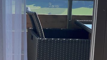 Un balcón con vistas a un paisaje, una silla de mimbre y una ventana que da al campo.