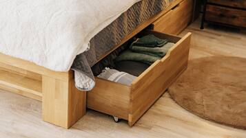 A bed with a wooden frame, a white blanket, and a drawer with folded clothes.