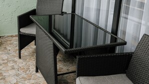 Un petit espace extérieur aménagé avec des meubles en osier, une table en verre et un sol carrelé en pierre.