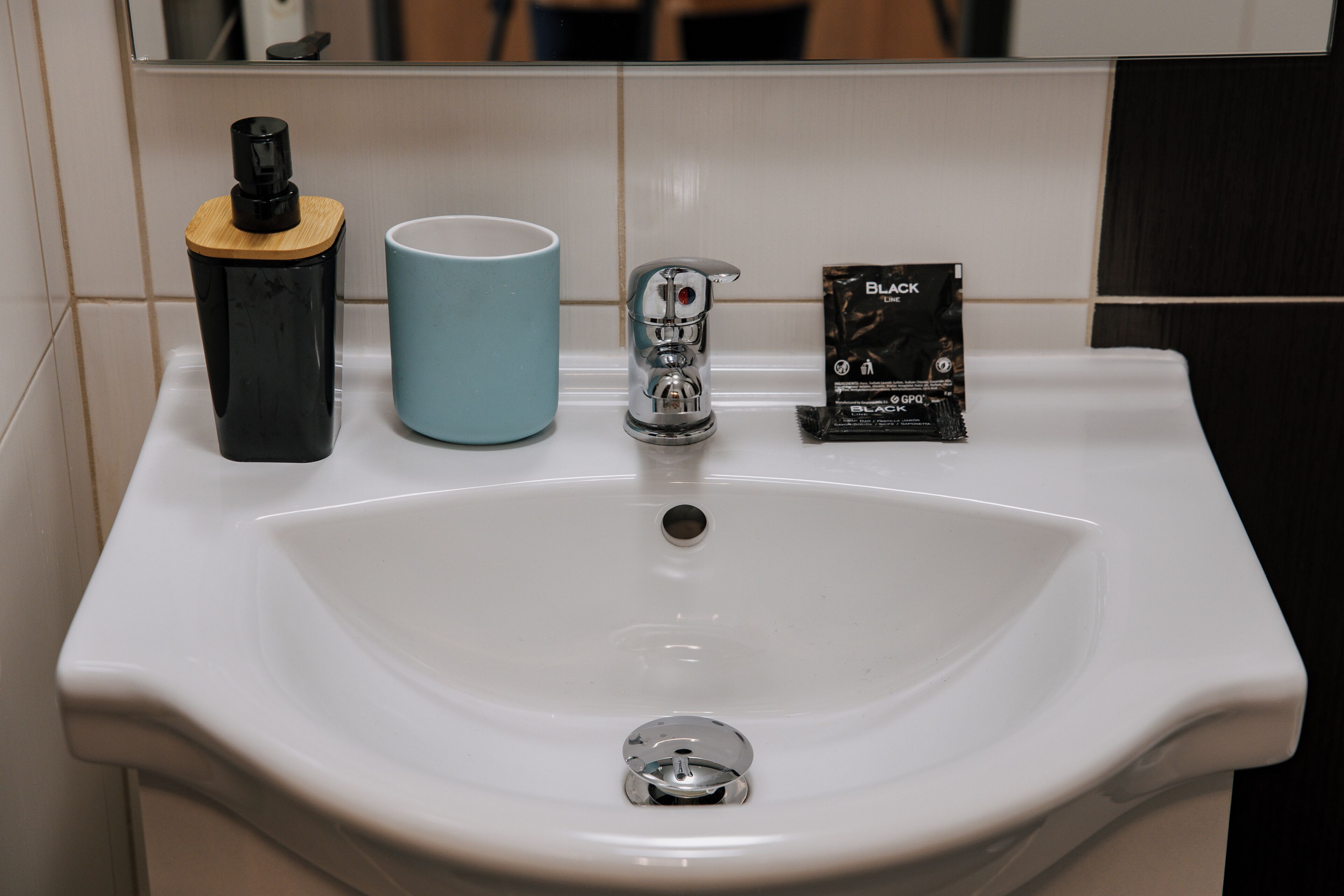 Un lavabo de salle de bain avec un robinet, une tasse bleue et un récipient noir.