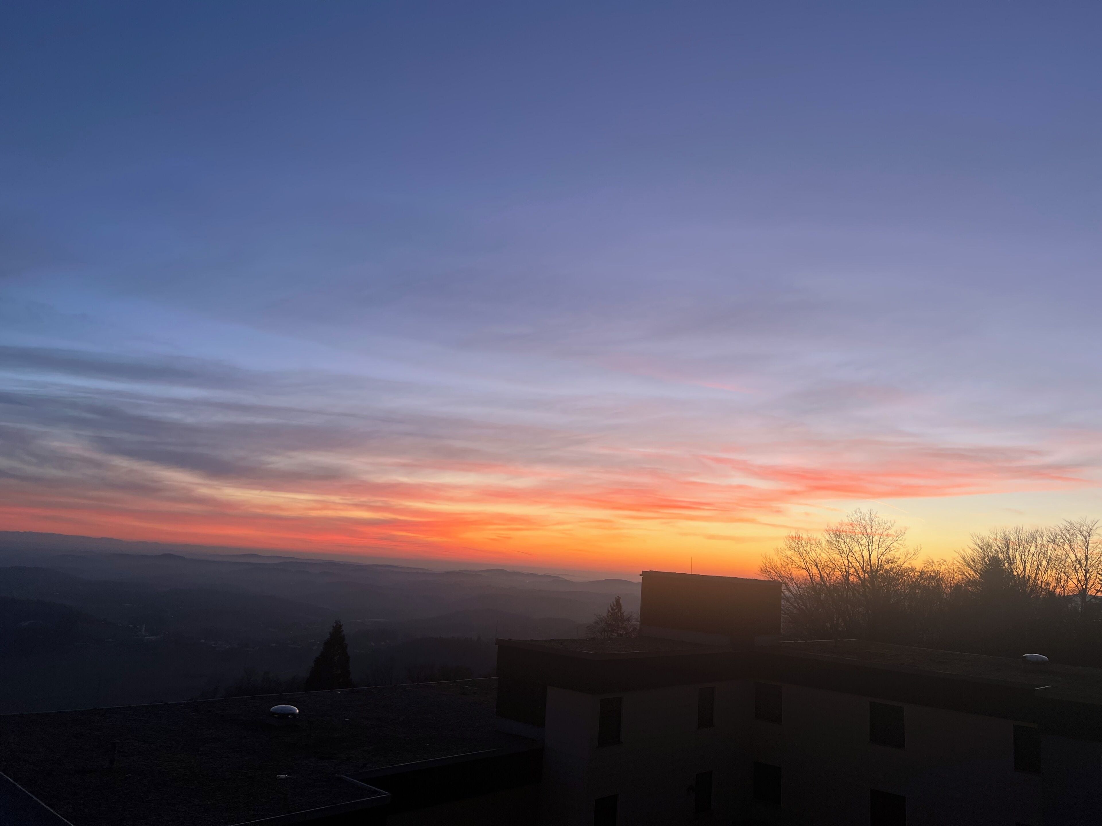 Ein Sonnenuntergang über einer Stadtlandschaft mit Gebäuden und einer fernen Bergkette.