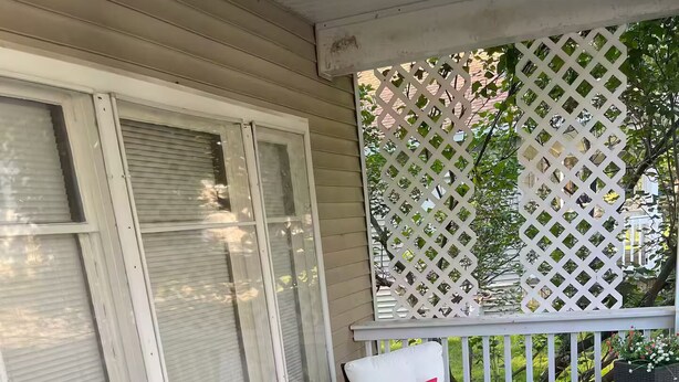 Un portico coperto con due sedie, un tavolo, un pannello a griglia e una pianta in vaso.