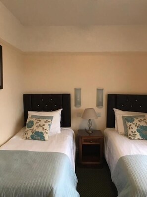 Une chambre d’hôtel avec deux lits, une table de chevet, une lampe et un luminaire fixé au mur.