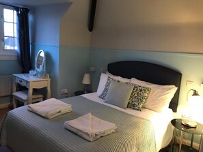 Ein Hotelzimmer mit Bett, Nachttisch, Lampe und einem Fenster mit Vorhängen.