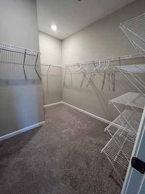 A laundry room with metal drying racks, carpeted floor, and a corner with a ceiling light.