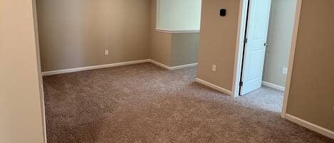 A room with beige walls, a carpeted floor, a door, and recessed lighting.