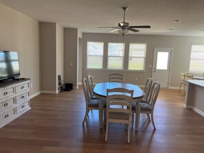 A dining area with a round table, six chairs, a ceiling fan, and a television on a dresser.