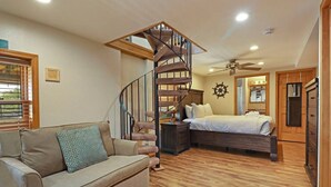 Une chambre avec un plancher en bois, un lit, une table de chevet, une commode et un escalier en colimaçon.