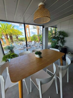 Uma área de refeições moderna com mesa de madeira, cadeiras brancas e luminária pendente.