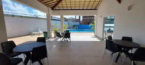 Eine Terrasse im Freien mit Pool, umgeben von Tischen und Stühlen, mit Blick auf die Nachbarschaft.
