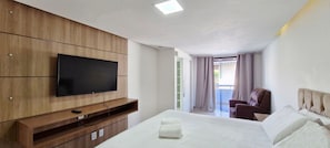 Ein Hotelzimmer mit Bett, einem an einer Holzvertäfelung befestigten Fernseher, einem Sessel und Blick ins Freie.