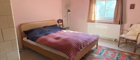 Une chambre à coucher comprenant un lit, une chaise, un radiateur, une fenêtre avec des rideaux et un luminaire suspendu.