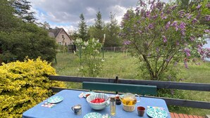 Ein Tisch im Freien mit blauer Tischdecke, Tellern, Besteck, einer Tasse und einer Karaffe.