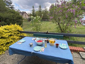 Ein Tisch im Freien mit blauer Tischdecke, Tellern, Besteck, einer Tasse und einer Karaffe.