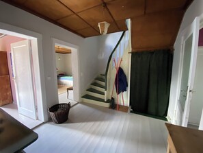 Una habitación con una escalera, una cama, una cesta y una puerta que da a otra estancia.