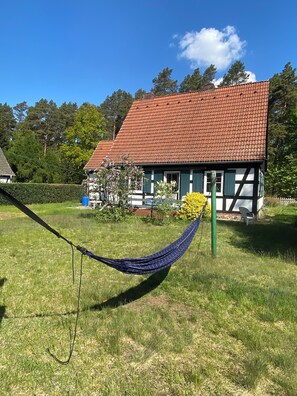 Una casa con techo de tejas rojas, un jardín con una hamaca y una silla.