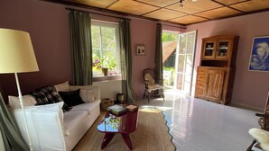 Ein Wohnzimmer mit einem weißen Sofa, einem roten Couchtisch, einer Lampe, einem Holzkabinett und Blick ins Freie durch ein Fenster.