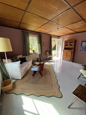Ein Wohnzimmer mit einem weißen Sofa, einem roten Couchtisch, einer Lampe, einem Holzkabinett und Blick ins Freie durch ein Fenster.
