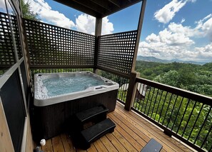 Uma banheira de hidromassagem em um deck de madeira com vista para uma paisagem arborizada.