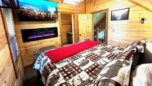 A wooden cabin bedroom with a bed, a fireplace, a ceiling fan, and a TV mounted on the wall. - Views from Deck-Hot Tub, game room, 5 min to parkway and attractions. (Pigeon Forge)
