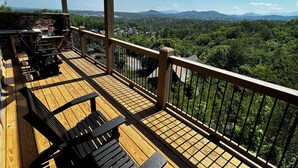 A wooden deck with outdoor furniture, a stone wall, and a view of a forested landscape with mountains in the distance. - Views from Deck-Hot Tub, game room, 5 min to parkway and attractions. (Pigeon Forge)