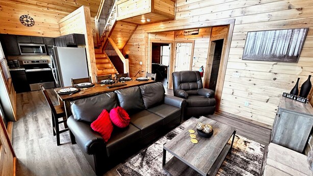 A cabin interior with a dining area, sofa, armchair, and a staircase. - Views from Deck-Hot Tub, game room, 5 min to parkway and attractions. (Pigeon Forge)