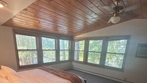 A bedroom with a bed, a ceiling fan, and large windows.