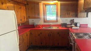 A compact kitchen with wooden cabinets, a red countertop, a window, and a stainless steel stove.