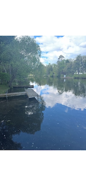 A calm lake with a dock extending into the water, surrounded by trees and a clear sky.